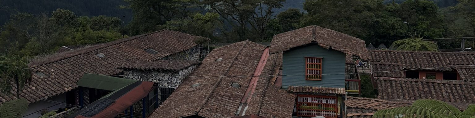 Clay-tiled rooftops stacked down a green hillside, one house painted teal
